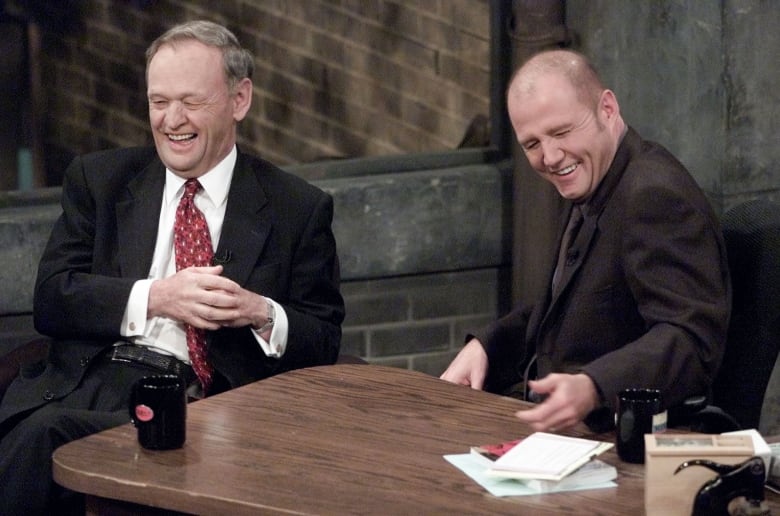 Two people laugh during a talk show interview.