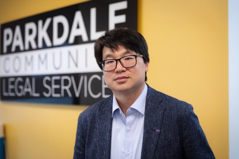 Lawyer John No stands in front of a sign for Parkdale Community Legal Services in the legal clinics office.