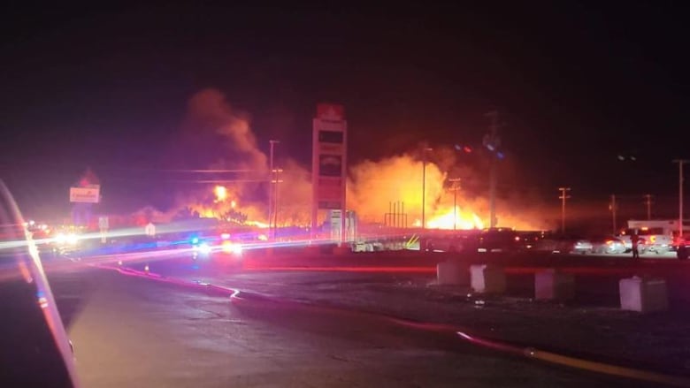 a fire is burning in the background and there is a gas station in frame