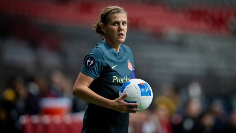 A soccer player gathers the ball in her hands for a throw-in