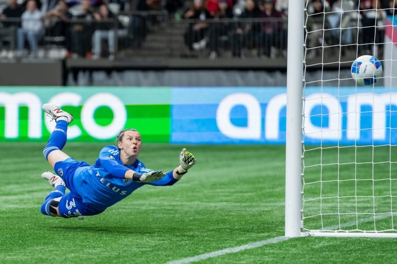 A soccer goalie watches in despair as a ball flies past her into the net.