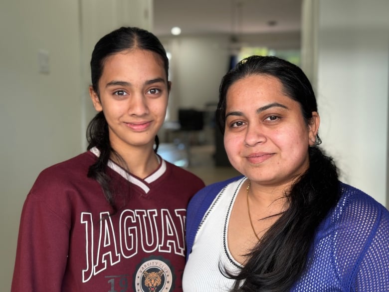 A teenager and her mother are shown at the front door of their home smiling.