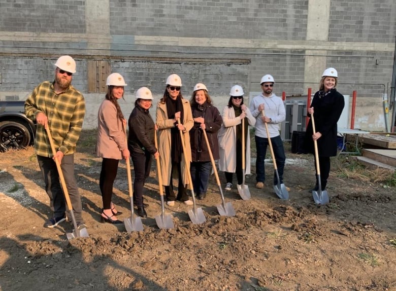 A group pf people are standing in a plot of dirt posing with shovels and wearing hardhats. 