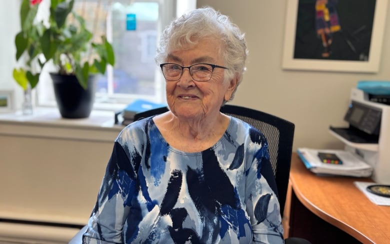 A woman with white hair sits at a desk.