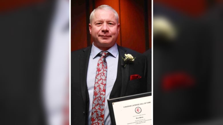 A man in his 50s with short grey hair and a suit holds an award.