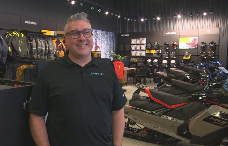 A man stands in a snowmobile showroom, grinning widely.