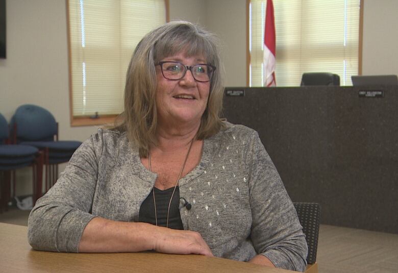 A woman sits at a boardroom table, a Canadian flag in the background.