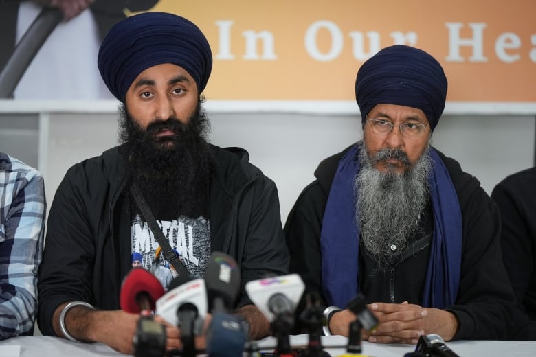 Two Sikh men with turbans speak at a news conference.