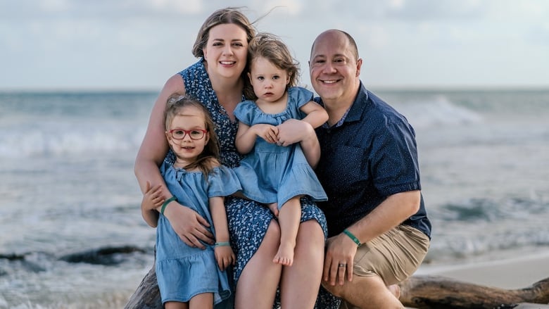 A family of four in blue clothing poses in front of an ocean.