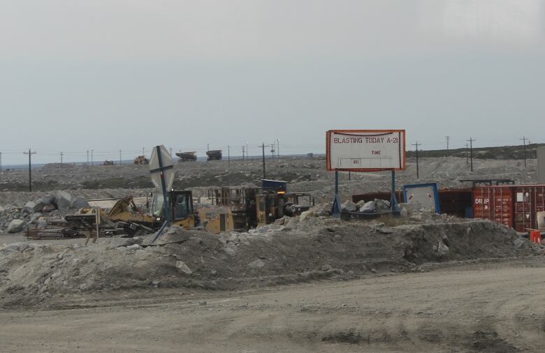 A sign in a rocky grey environment, surrounded by machinery.