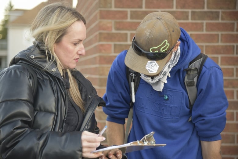 A woman stands next to a man with his face obscured. 