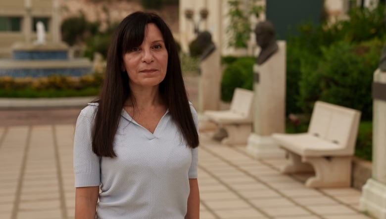 A woman standing in a plaza, wearing a light top, poses for a photo.