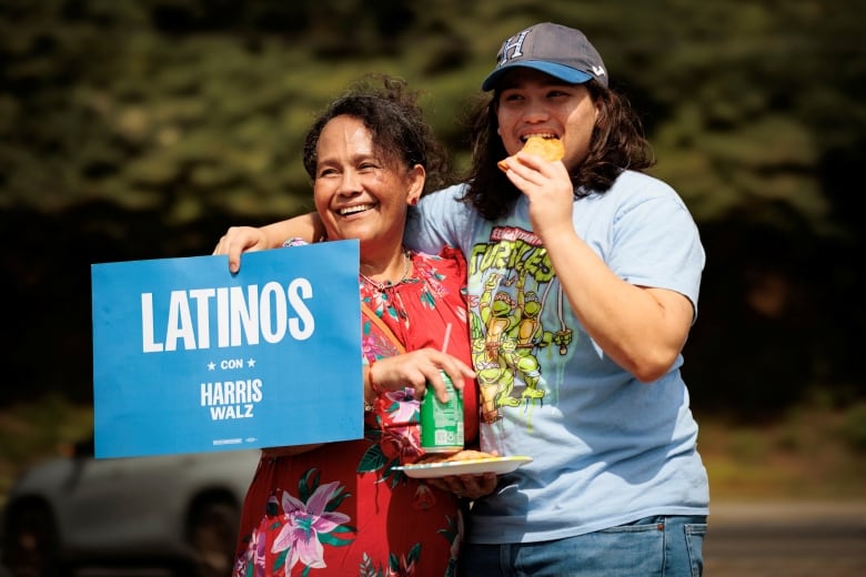 Two women hold a Latinos con Harris Walz