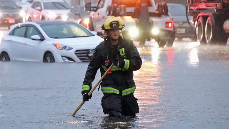 A firefighter stands in a knee-deep flooded street. 