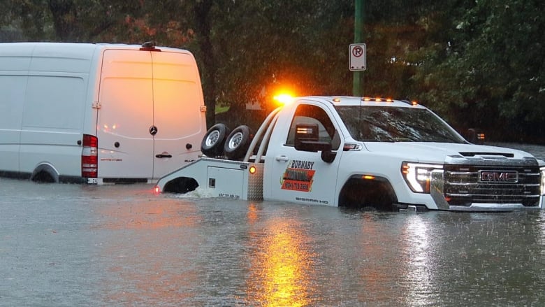 A tow truck tries to pull a white van from a flooded street.