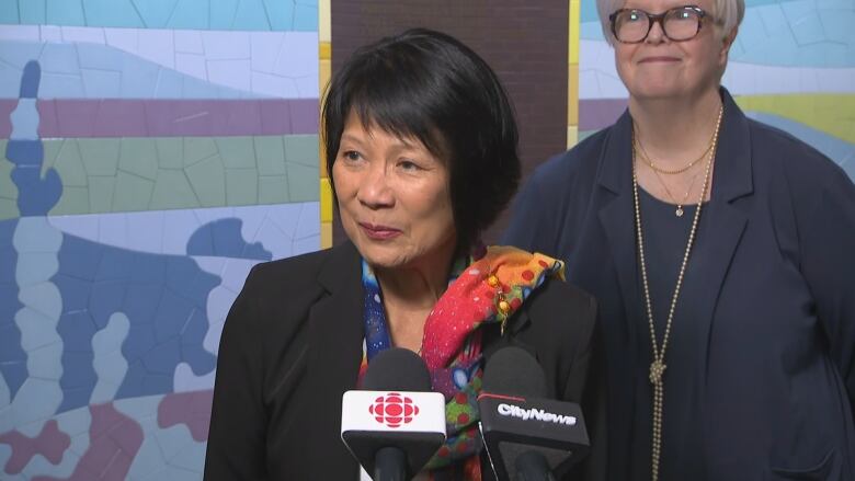 Toronto's mayor and a female city councillor stand at a lecturne full of microphones