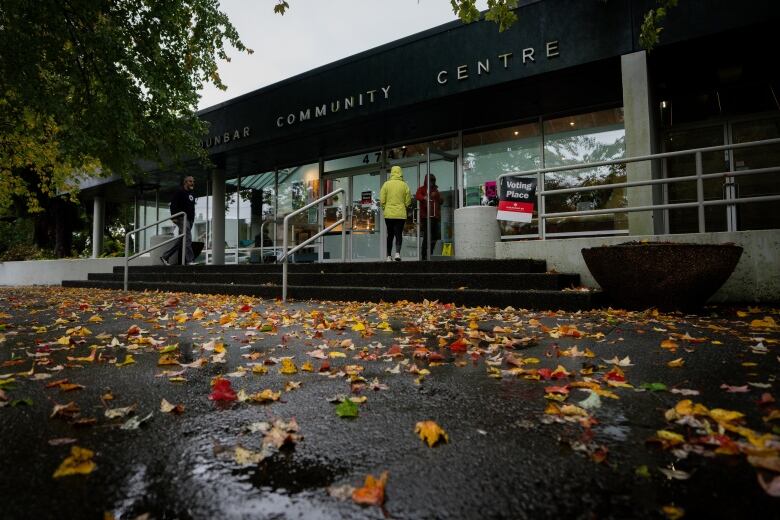 A person is seen from behind entering a community centre on a rainy day. 