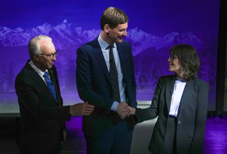 A woman shakes hands with a tall man, as another man reaches in for a handshake.