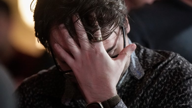 A man with short brown hair and black glasses holds his palm over his face during a close electoral race.