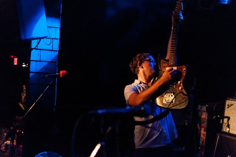 A man holds up an electric guitar on a dark stage.