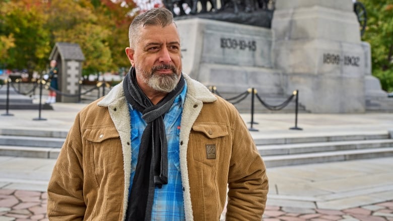 A man in a brown coat standing in front of the National War Memorial in Ottawa.