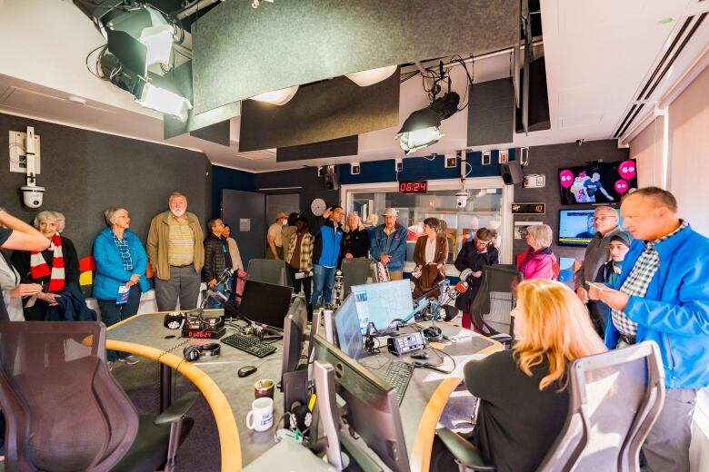 a crowd of adults stand around a desk in radio studio