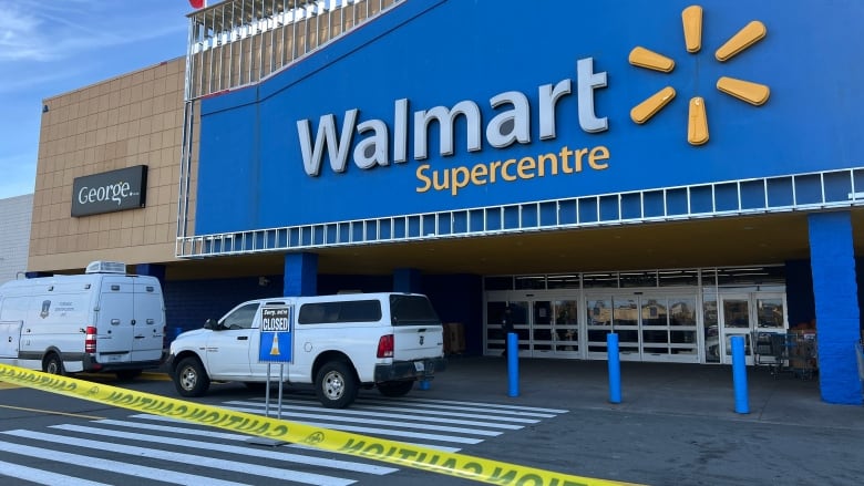 Police vehicles and caution tape are seen outside of the entrance of a Walmart. 