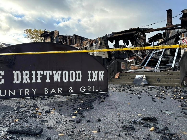 A sign for a hotel sits on the ground in front of a burned building. There's also police tape around the scene.