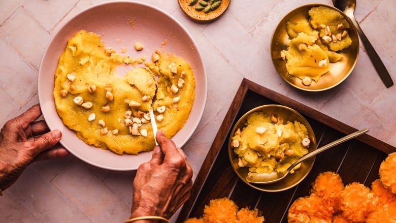 Overhead shot of hands scooping a spoonful of Kesari from a pink bowl. 2 small bowls of the dessert sit next to the big bowl. 