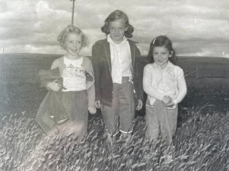 An old black and white photo of three girls in a field of tall grass. 