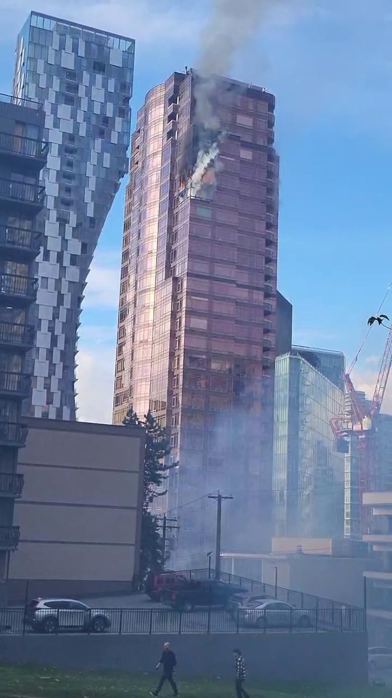 Several floors of an apartment highrise are pictured on fire on a sunny day.