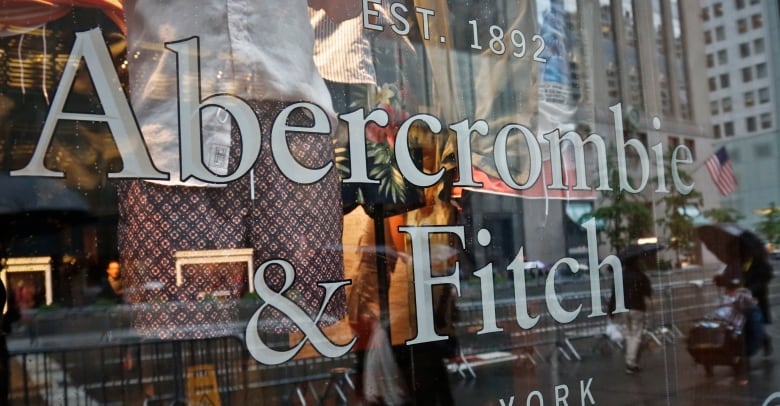 The lettering says Abercrombie & Fitch on a store window, with clothing visible behind it, as well as reflections of a city street. 