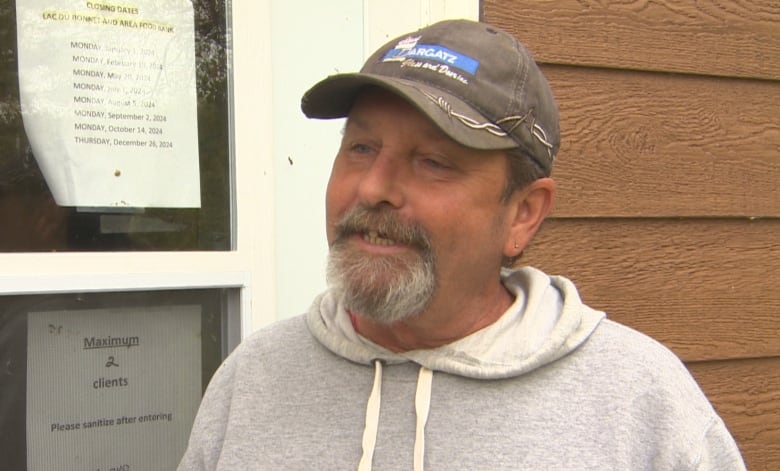 A man in a baseball cap smiles in front of the food bank door.