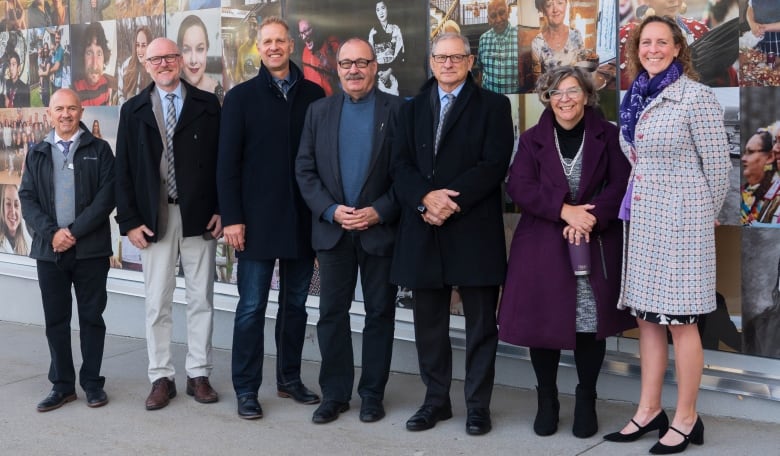 Seven people stand in front of a wall filled with various posters