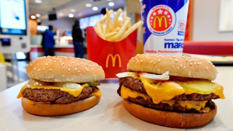 Two hamburgers sit on a table in front of a box of fries and a fountain pop. 