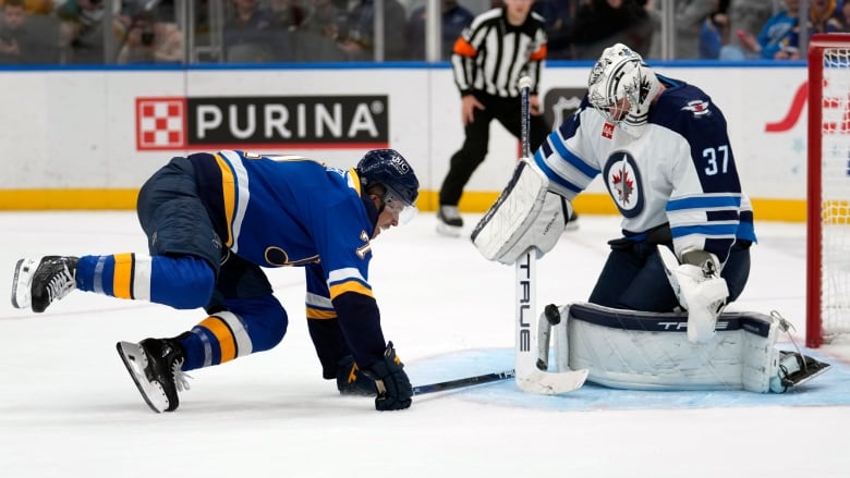 A hockey player falls as a goaltender for the opposing team deflects the puck from the net. 