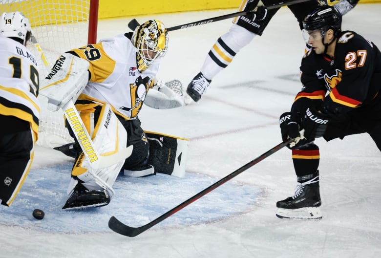 a hockey player in a dark uniform tries to get a puck past a goalie in white and yellow