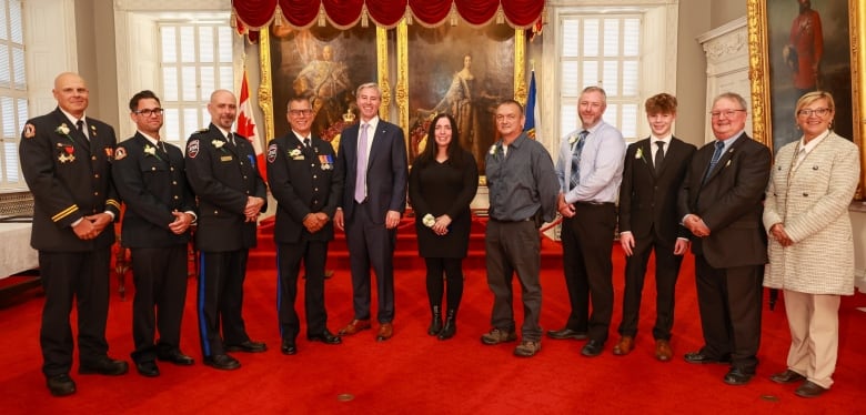 A group of people standing in a line in an ornate room, four of whom are wearing uniforms, the others are wearing suits. 