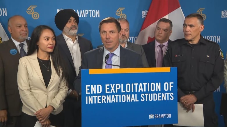 Brampton mayor Patrick Brown speaking to a microphone. Behind him are other city representatives and a blue backdrop that says 