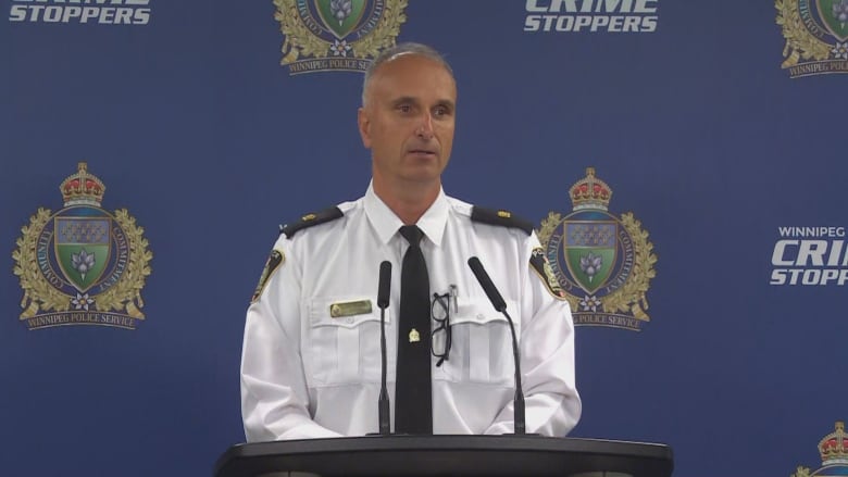 A police officer answers questions from reporters while standing at a podium. 