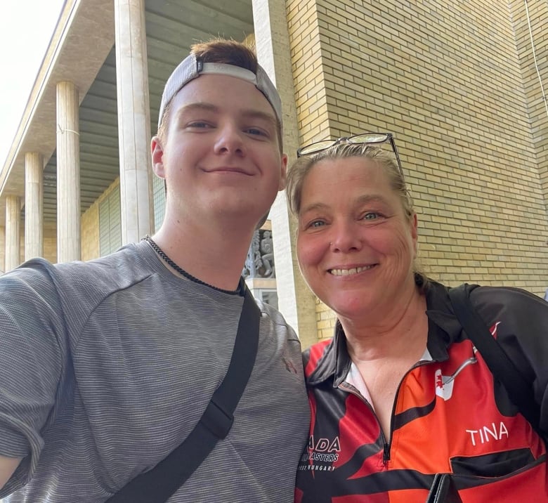 A teenager and a woman pose for a photo in front of a brick building with large entry pillars.