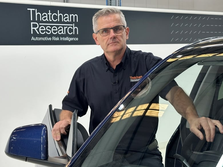 A man is stepping into the front seat of a car and looking at the camera.