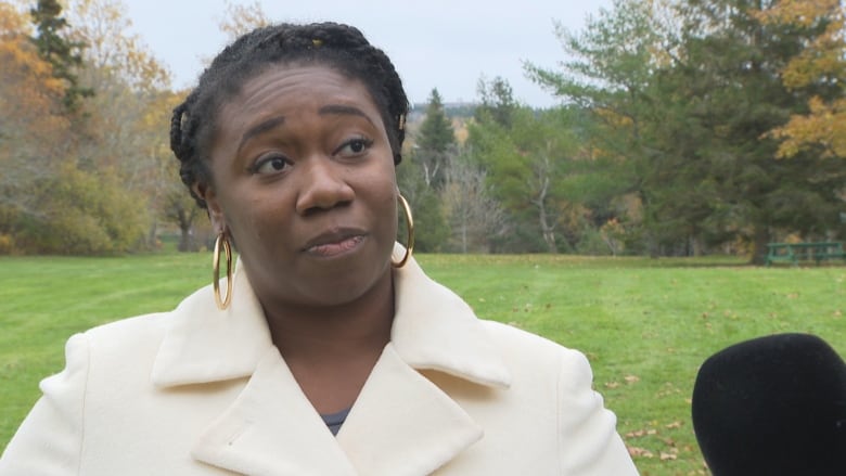 A woman wearing a white coat stands in a public park.