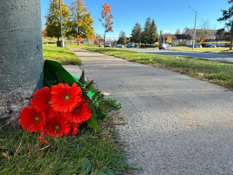 Red flowers sit next to a sidewalk. Police tape can be seen in the distance.