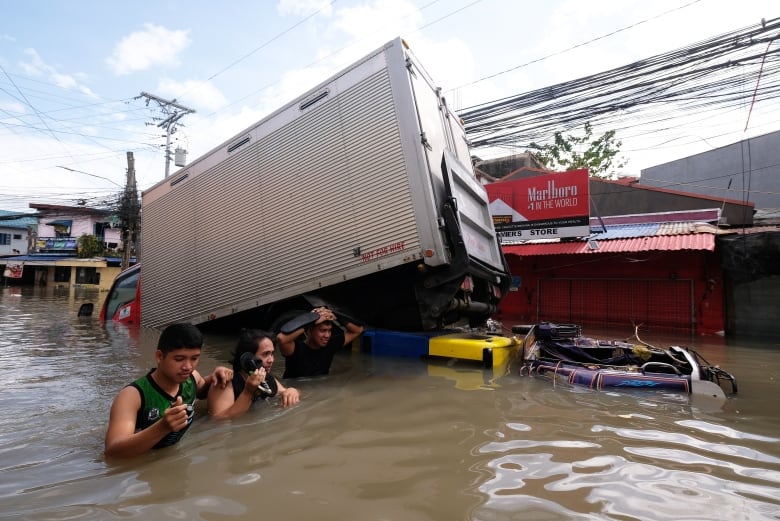 Several people are up to their chest or neck in murky brown water beside debris.