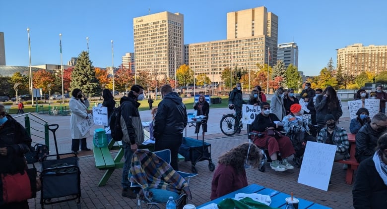 People in masks sitting and standing in front of Ottawa's City Hall.