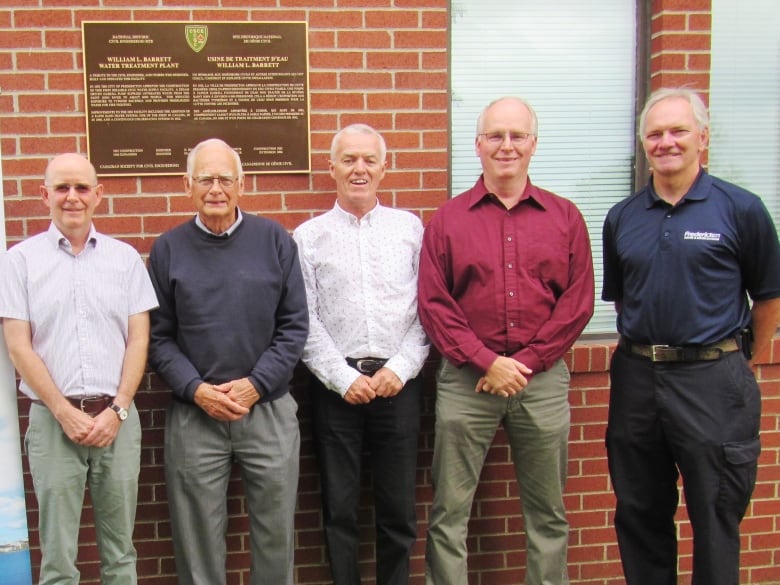 Five men standing next to each other against a brick wall