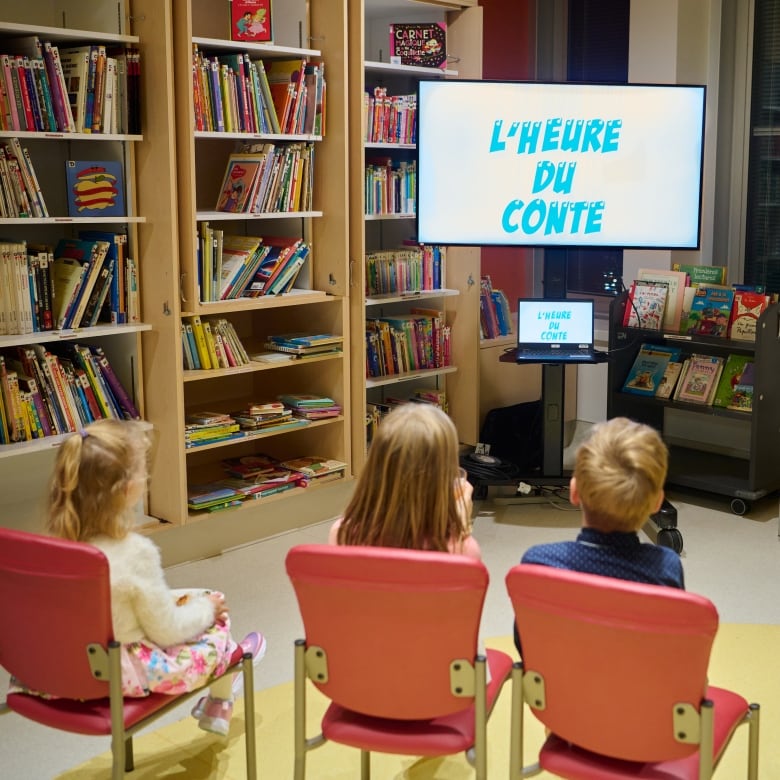 Kids sitting in chairs in front of a TV that says 