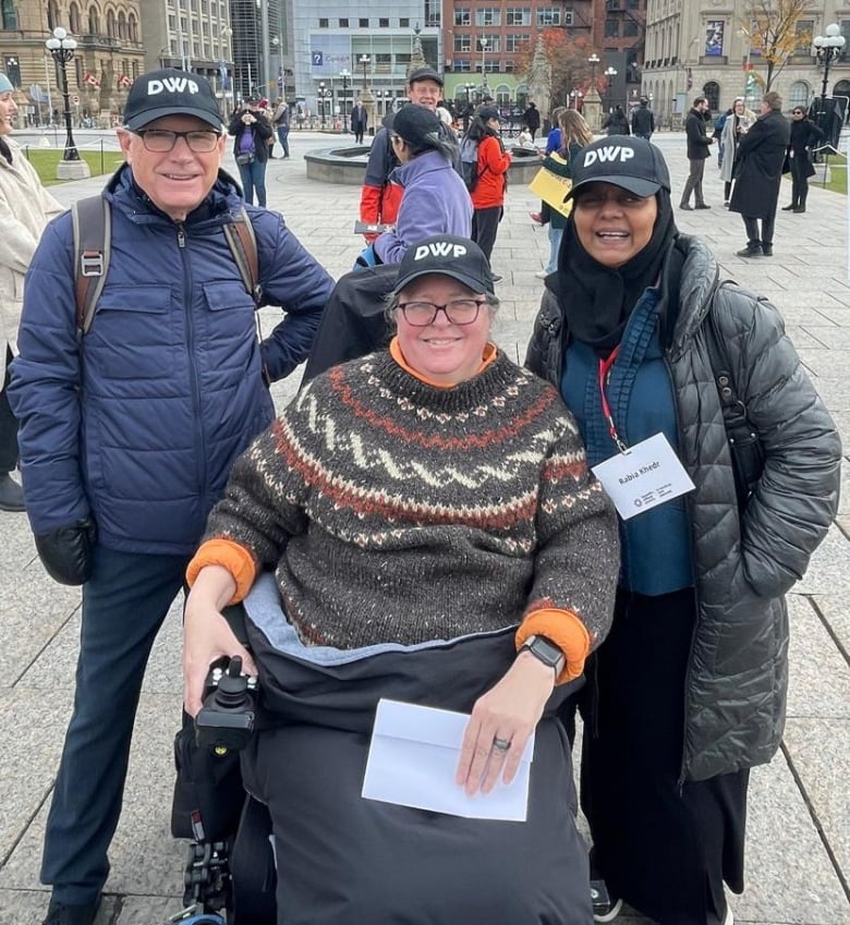 Three people pose for the camera. Two are standing, one is seated.