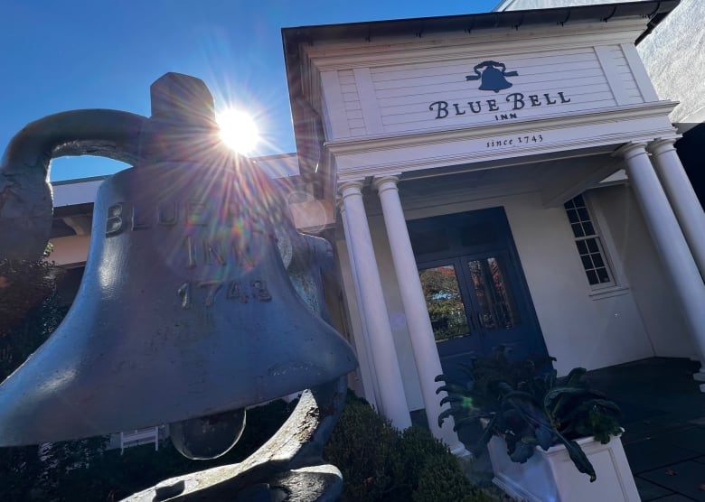 Blue bell in front of a white wooden building with pillars.